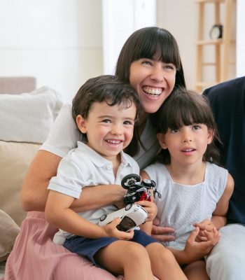 Cheerful funny parents and two kids watching funny movie at home, sitting on couch in living room and looking away and laughing. Medium shot. Leisure time with family or television concept